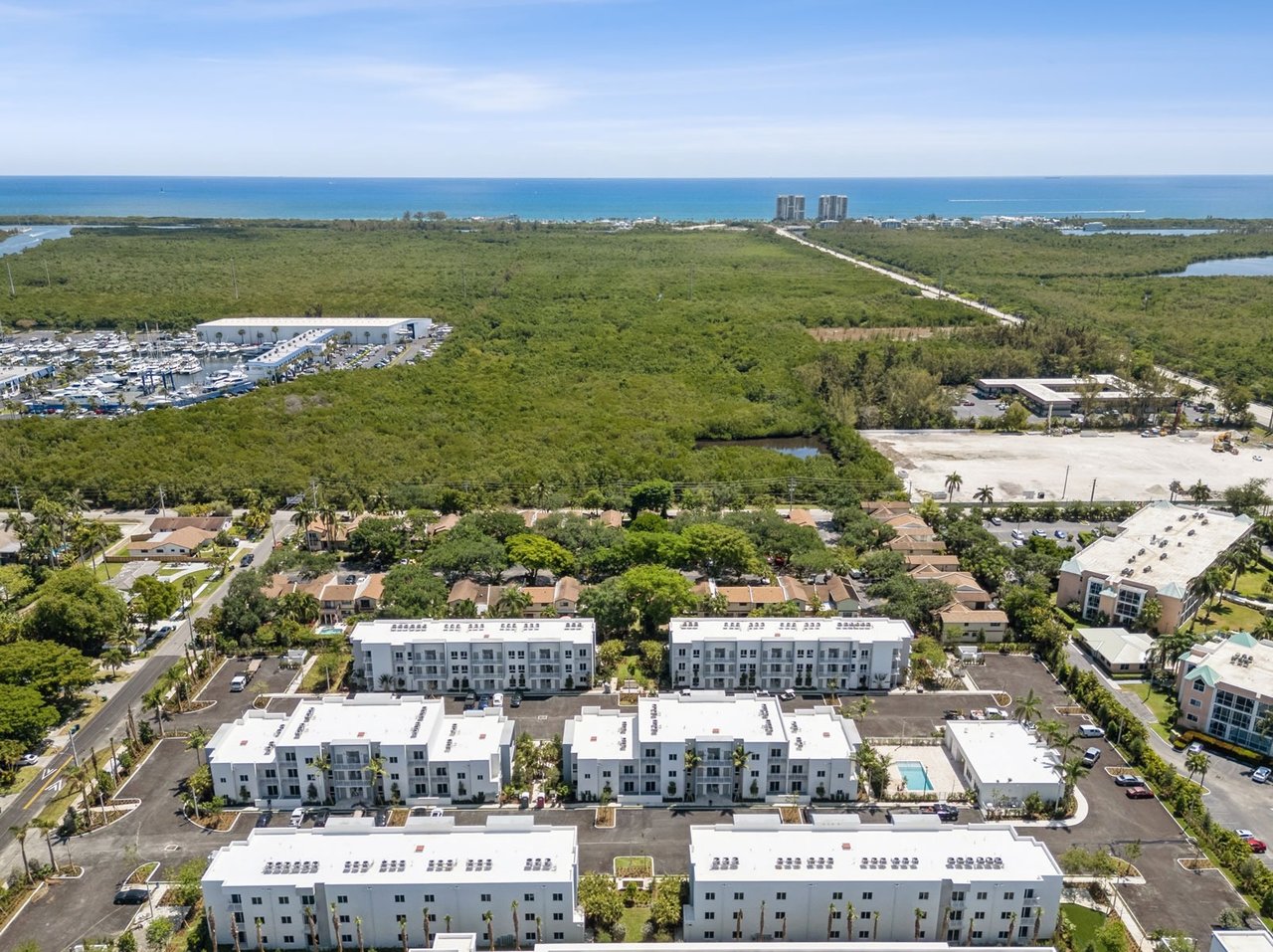 Aerial view of white residential buildings, green coastal wetlands, a marina, and the ocean.