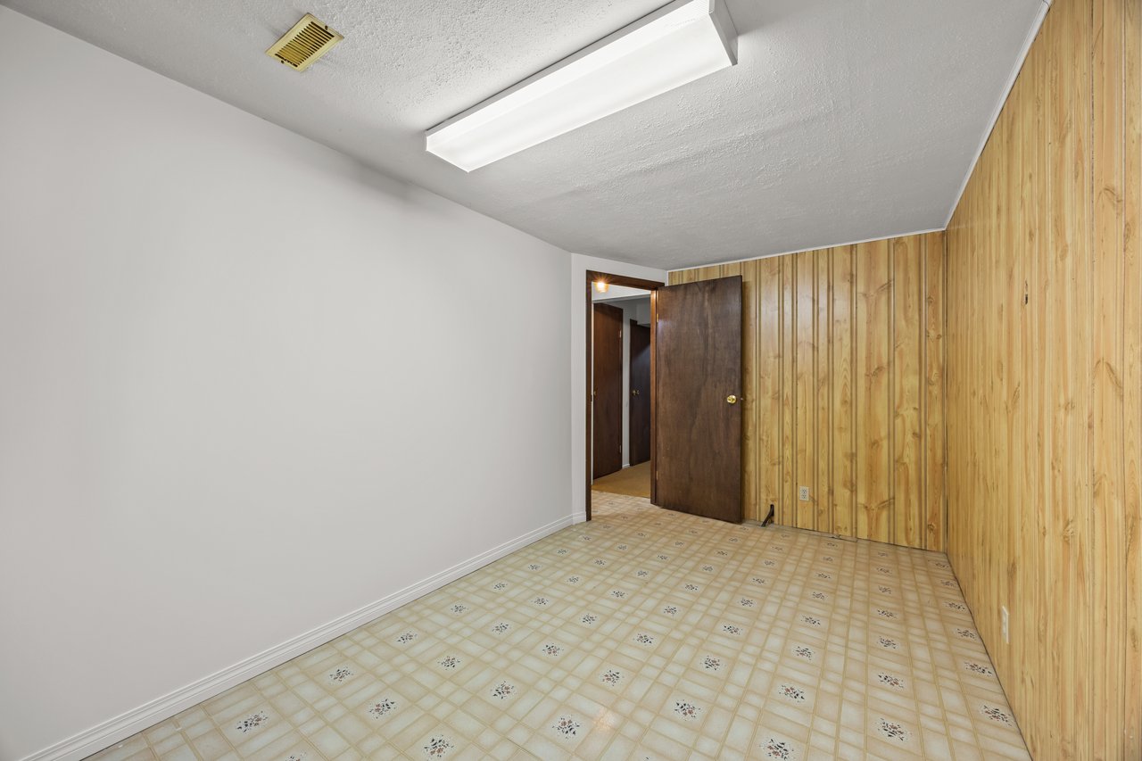Empty room with patterned linoleum, wood-paneled walls, and an open dark wooden door.