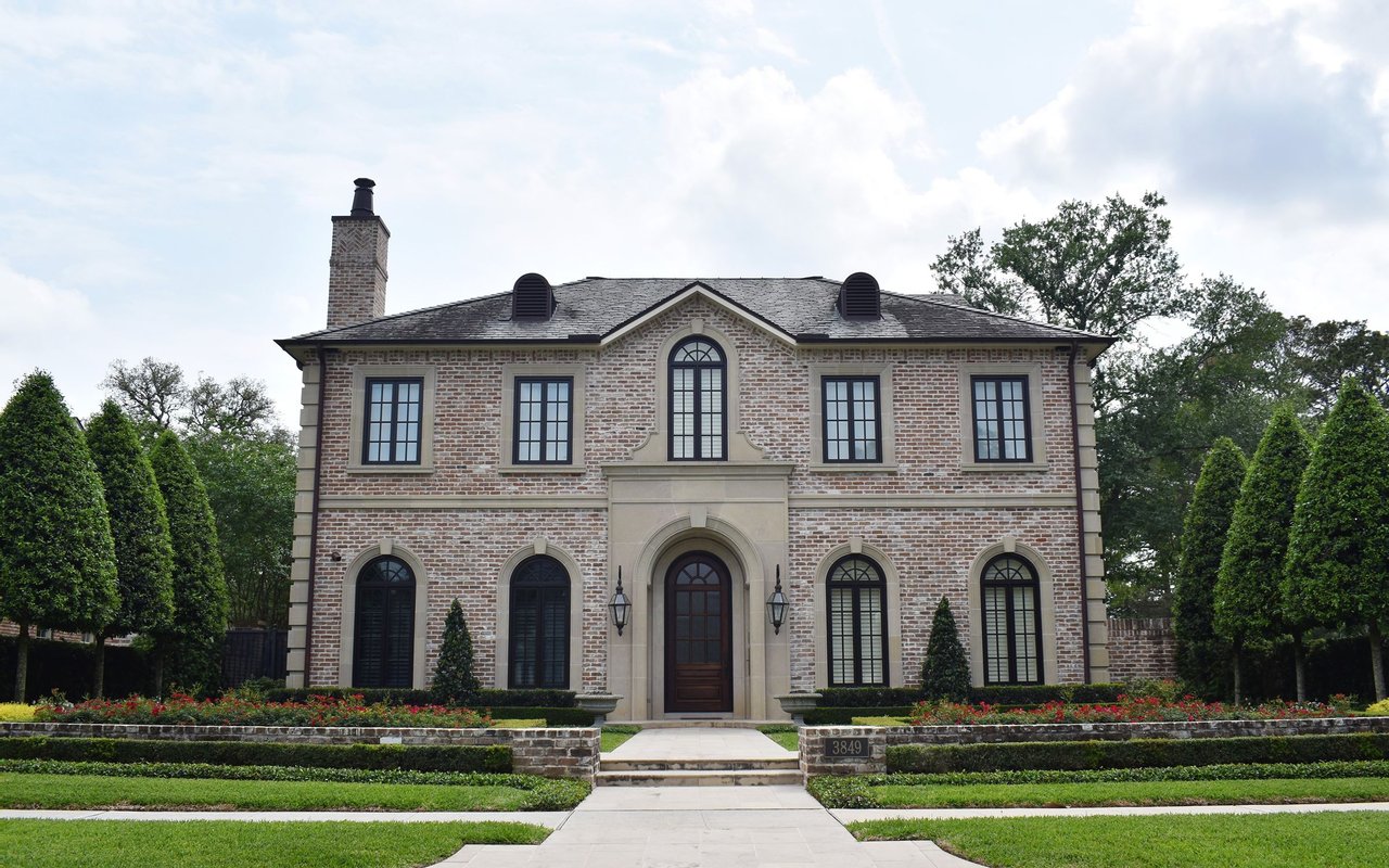 Two-story brick house with arched windows, a central stone entrance, and formal front gardens.
