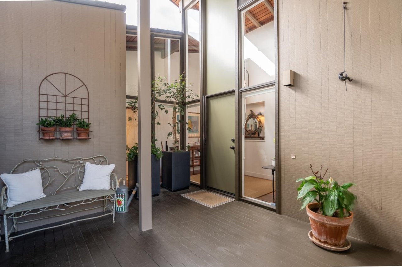 Covered courtyard patio with glass doors, potted plants, and a metal bench with white cushions.