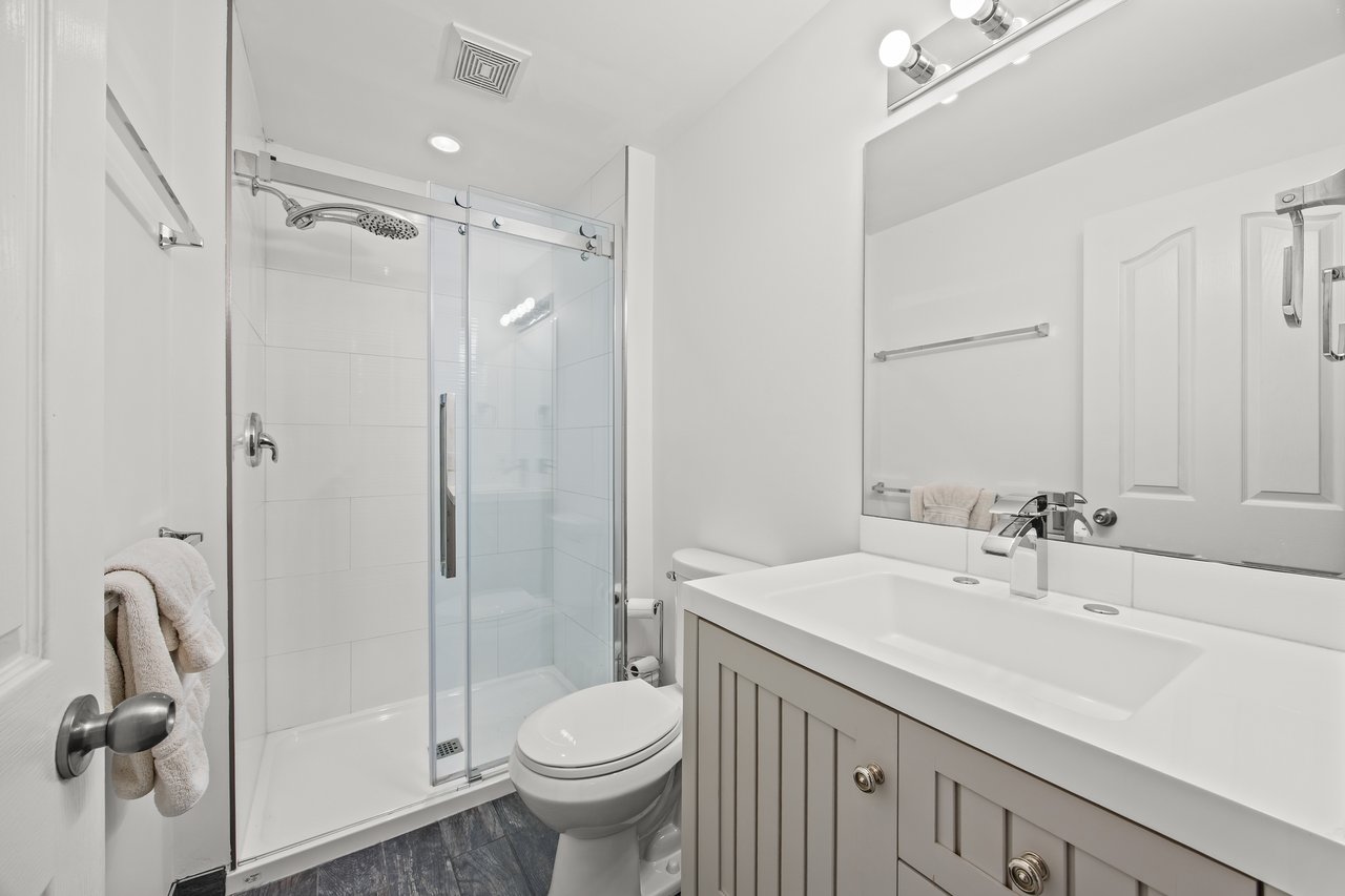 Bathroom with a glass-enclosed shower, toilet, and white vanity beneath a large mirror.