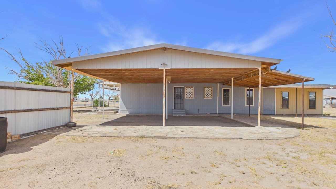 Single-story gray house with a wide covered carport and white metal fence.