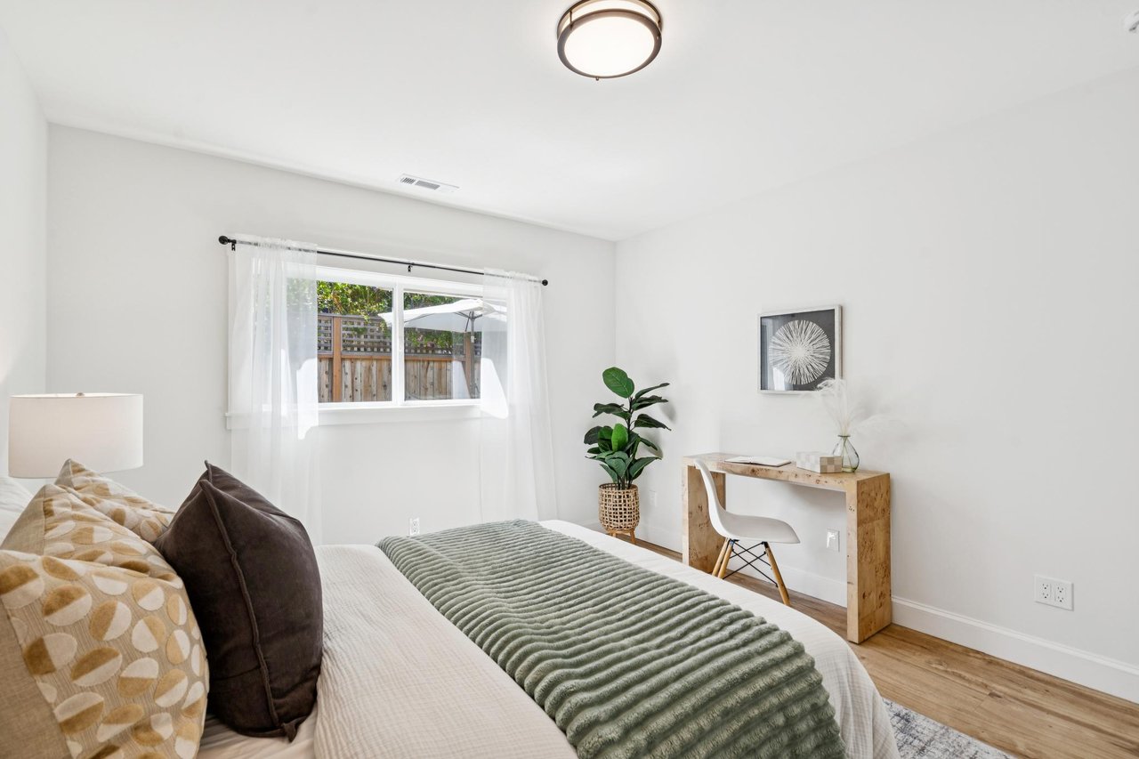 Staged bedroom with a bed, desk, and window overlooking a fenced yard.