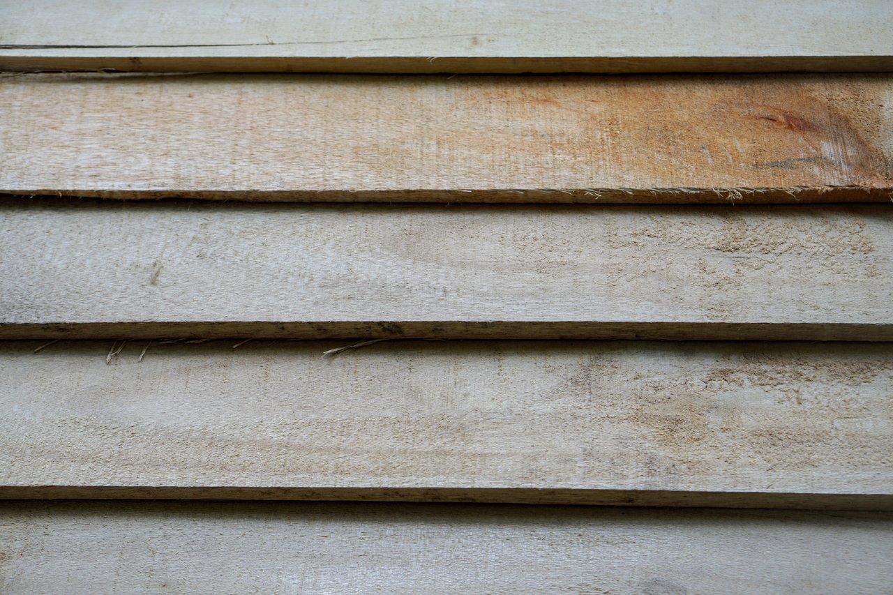 Weathered pale gray horizontal wood siding with visible grain and a brown-stained board.