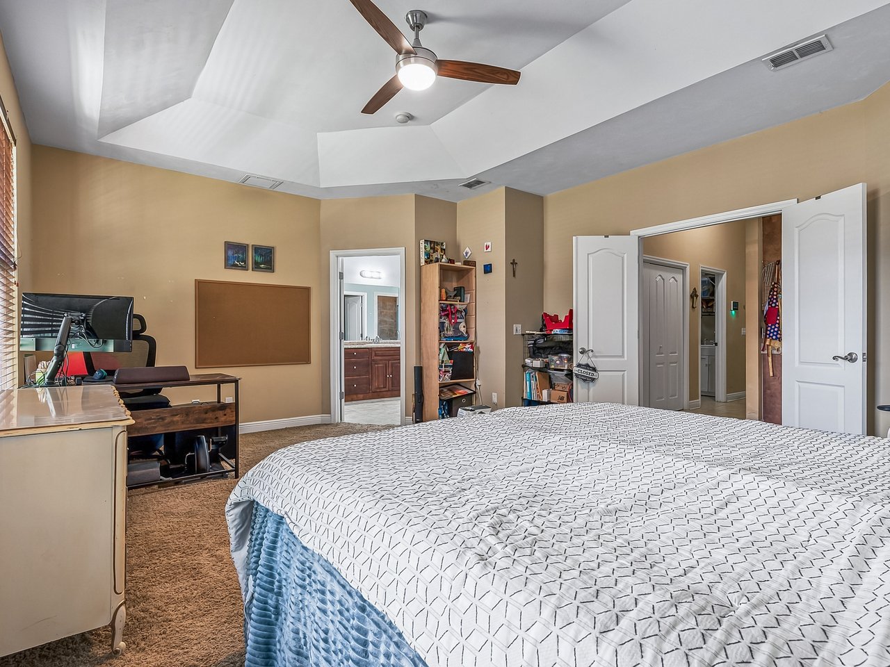 Furnished bedroom with a large bed beneath a vaulted ceiling and a desk by the window.