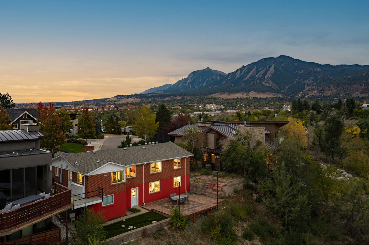 Rear of 2003 Balsam Drive at dusk showing the two-level brick exterior and patio with the Flatirons behind