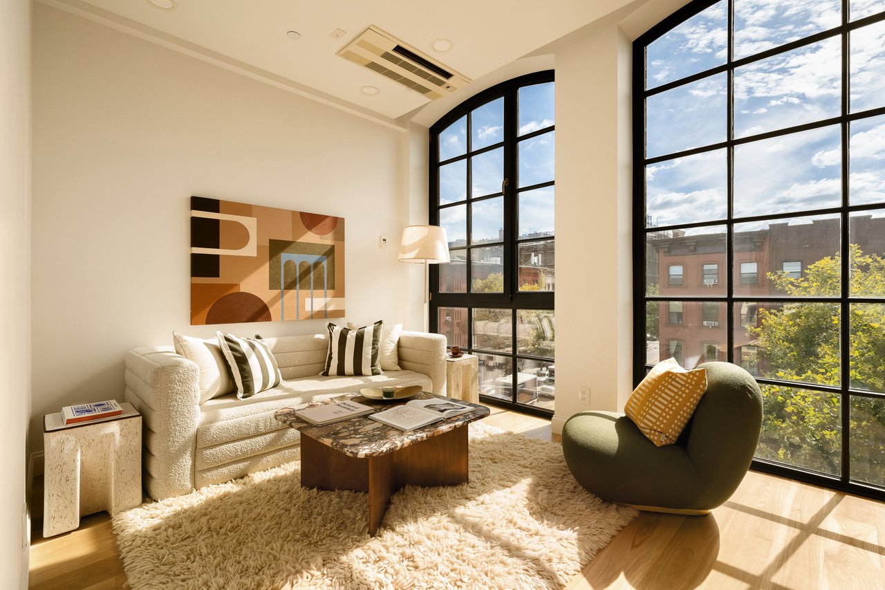 Staged living room with tall black-framed windows, a cream sofa, and a green armchair.