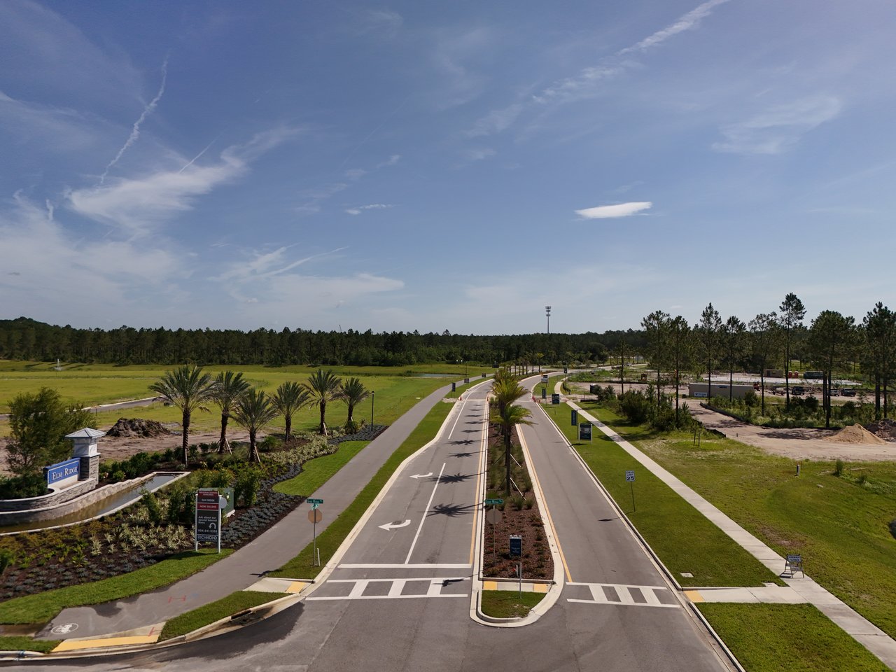Elm Ridge community entrance with landscaped roads, palm trees, and nearby construction.