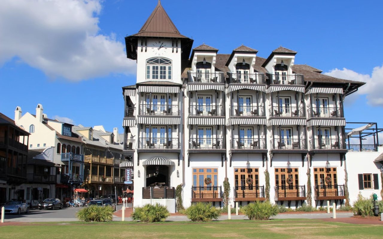 White streetfront building with a clock tower, multiple balconies, and striped awnings.