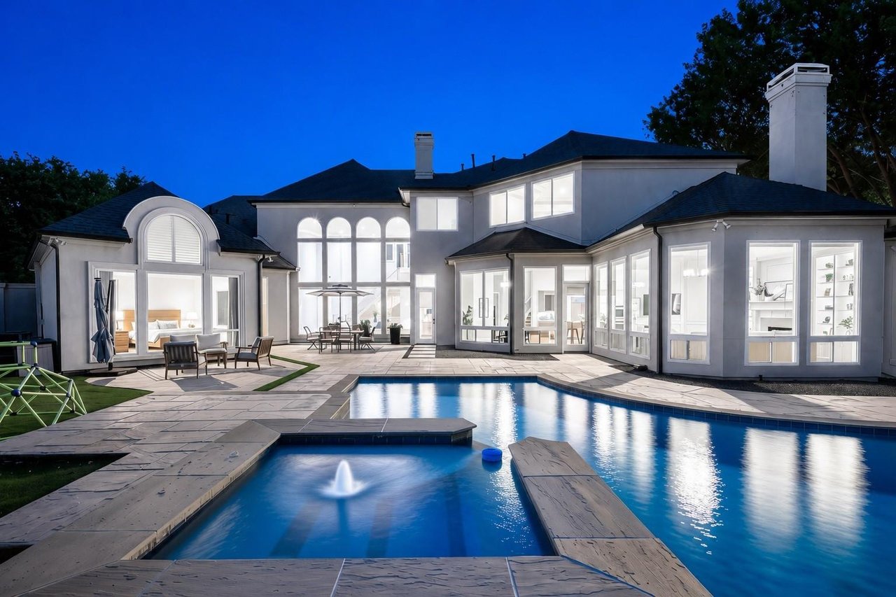 Large two-story home with illuminated windows, stone patio, and swimming pool at dusk.