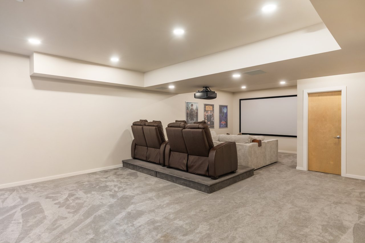 Lower-level theater with a tray ceiling, recessed lighting, and raised leather seating