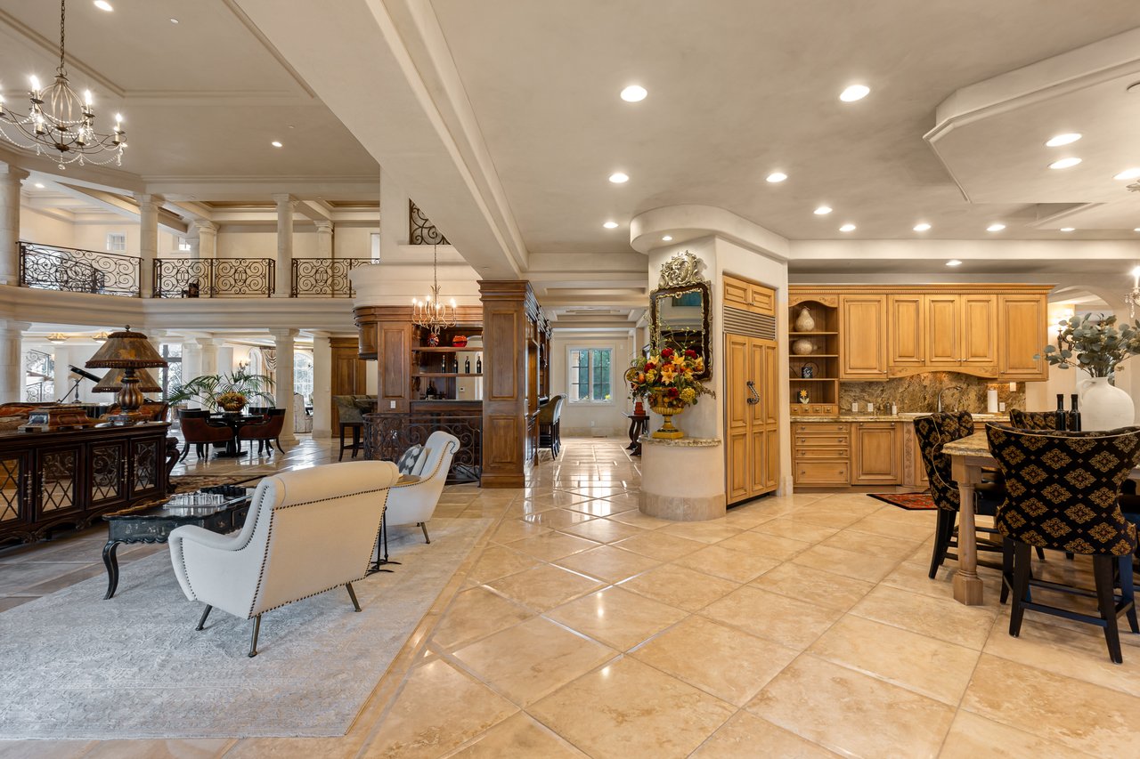 Open-plan living and dining area with wood cabinetry, tiled floors, and an ornate upper-level railing.