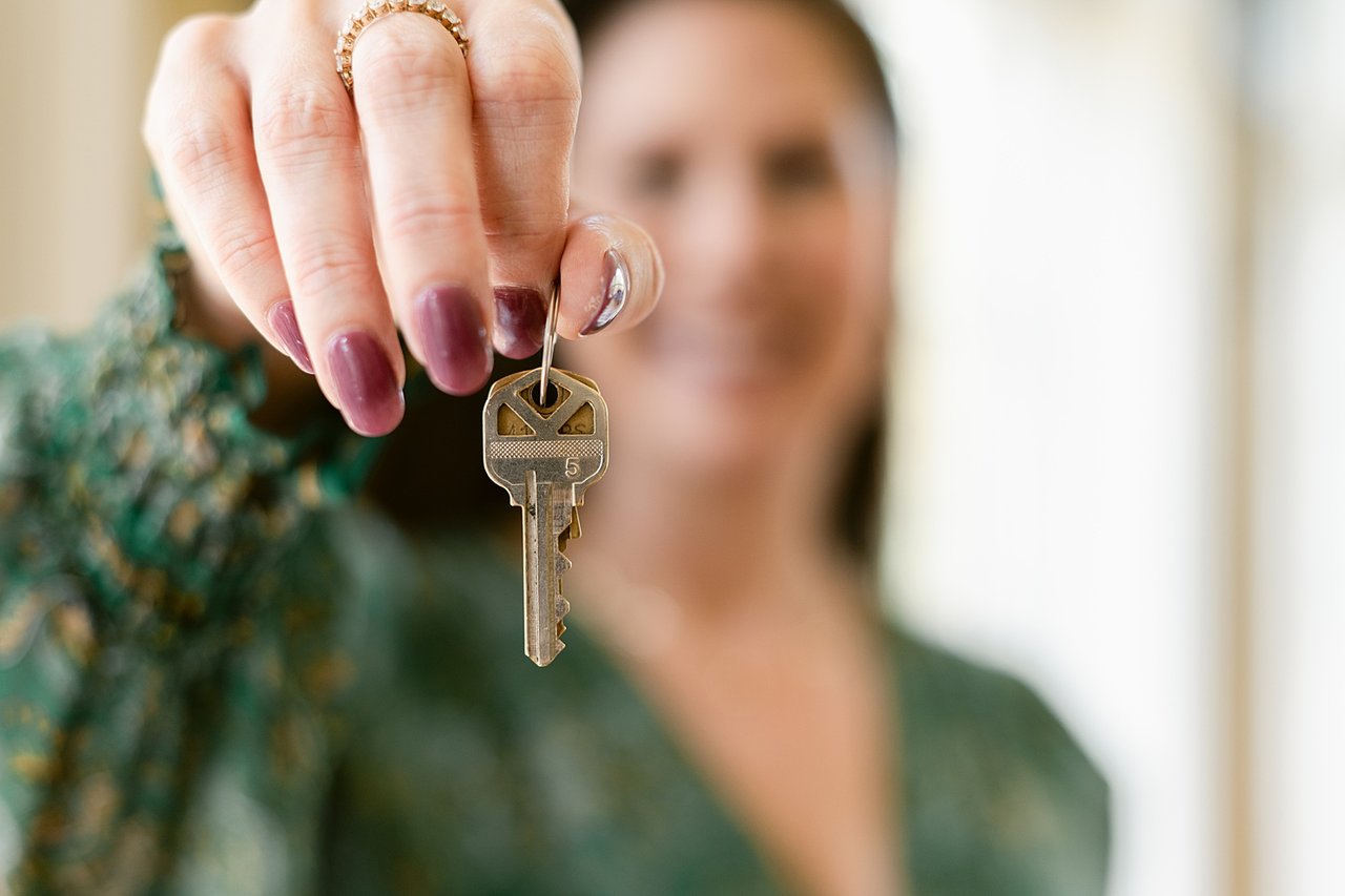 A woman holds a metal house key, her face blurred behind it.