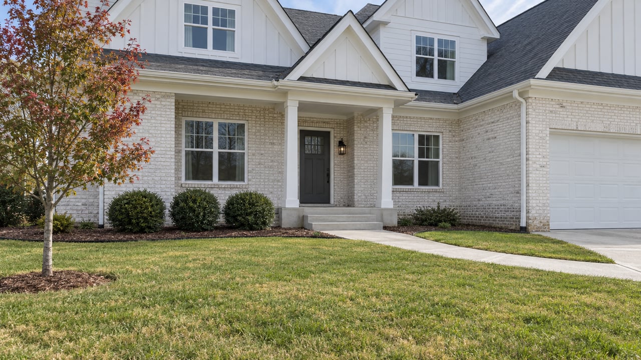 White brick and siding home with a recessed front porch, broad lawn, and a young red maple in early autumn.