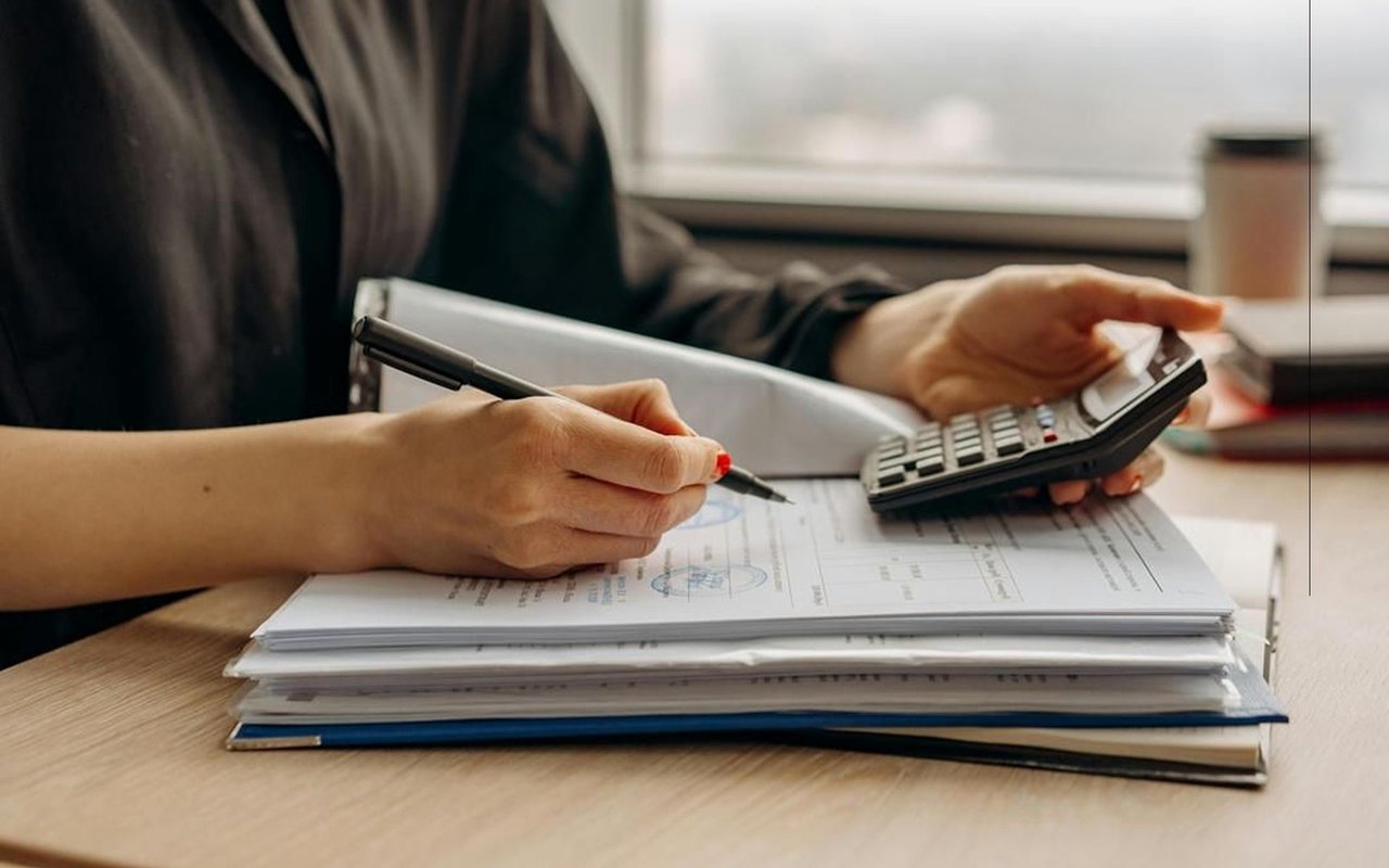 Person calculating figures and writing on financial paperwork at a desk.