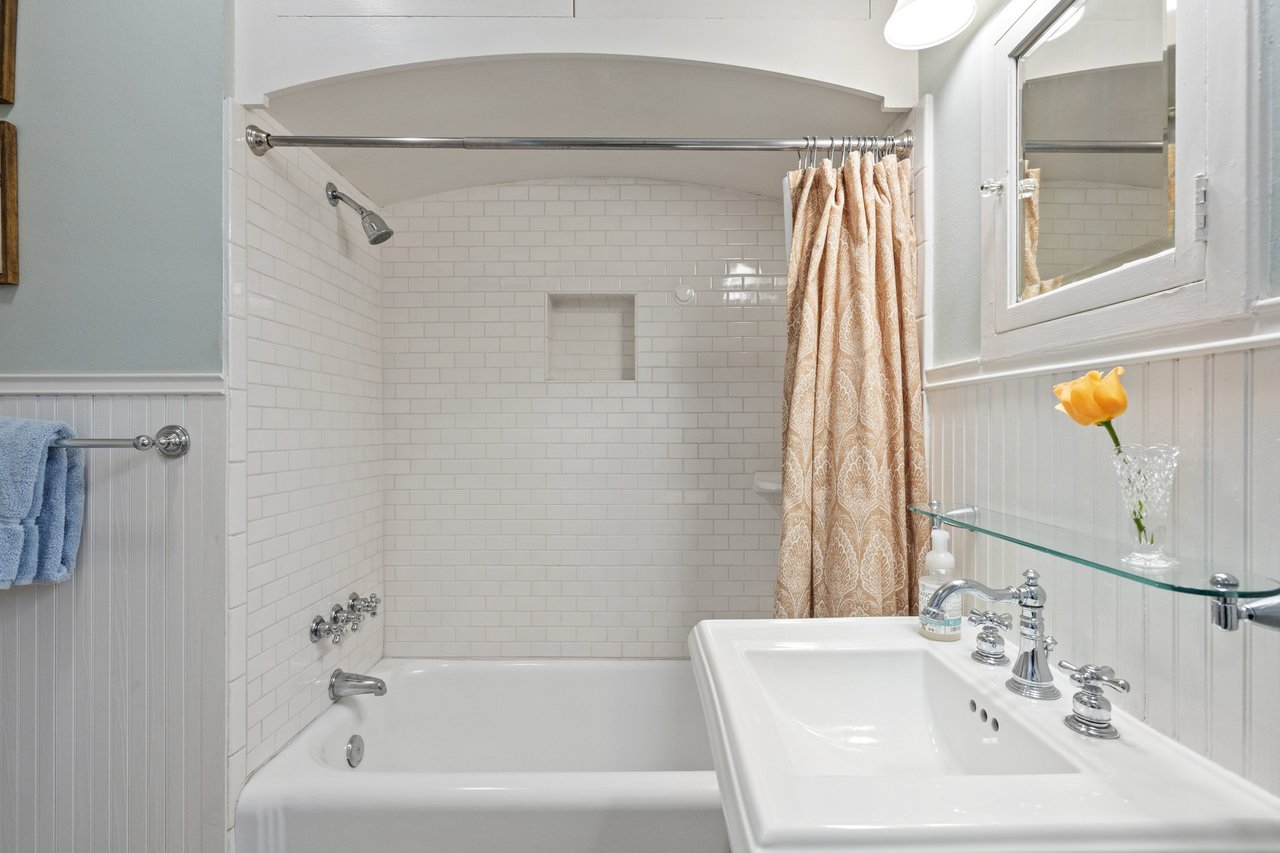 Bathroom with subway-tile tub, patterned shower curtain, and white sink with chrome fixtures.