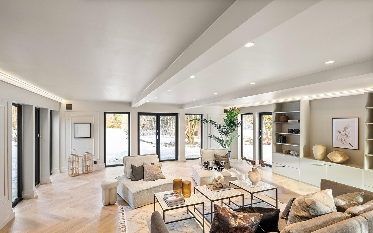 Modern living room with pale furnishings, built-in shelving, and large windows overlooking snow.