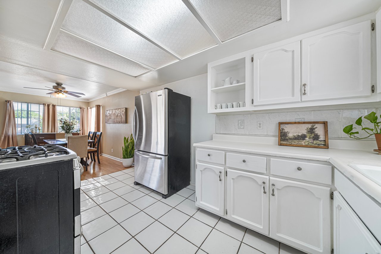 Kitchen with white cabinetry, stainless steel refrigerator, and black gas range opening to a dining area.