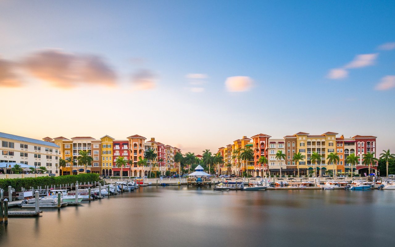 Waterfront marina lined with colorful buildings and boats beneath a warm sunset sky.