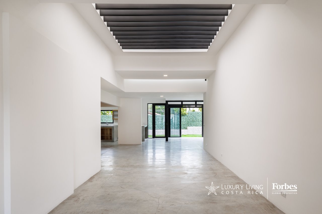 Vacant living area with polished concrete floors, exposed ceiling beams, and garden-facing glass doors.