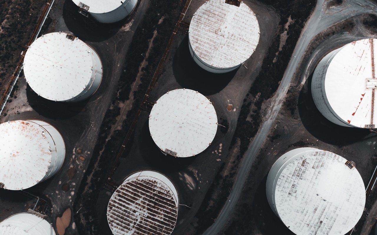 Aerial view of large round storage tanks arranged along industrial service roads.