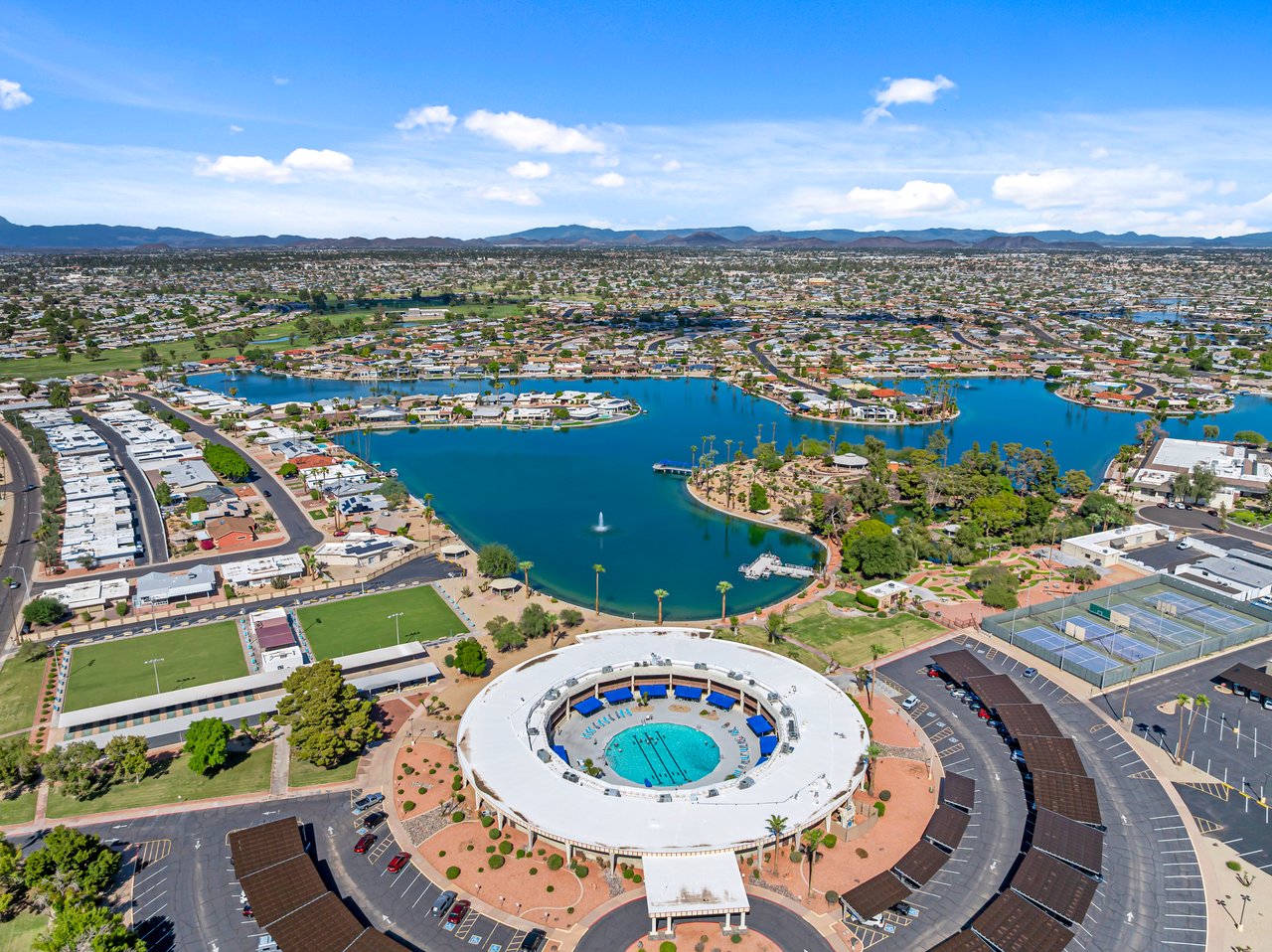 Sun City neighborhood with a large recreation center, lake, and mountain horizon.