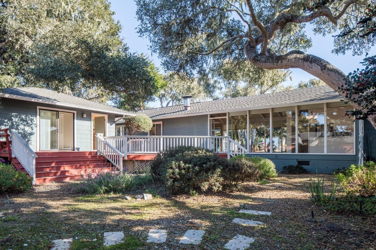 Single-story home with a red entry deck, white railings, and mature trees.