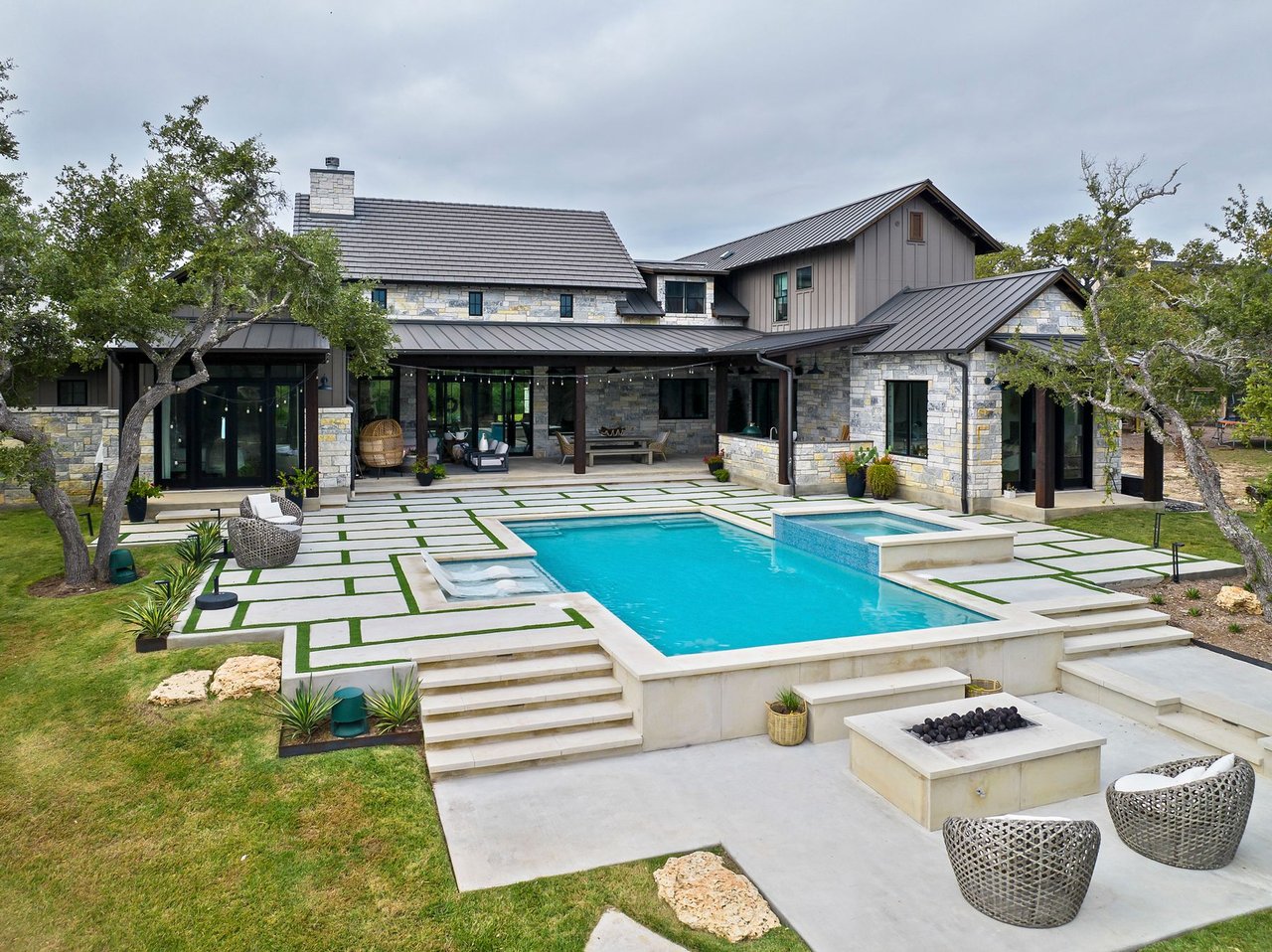 Rear exterior view of this Creek Road Ranch home in Dripping Springs, Texas, showing the pool, spa, and firepit patio, designed by architect Kai Geschke.