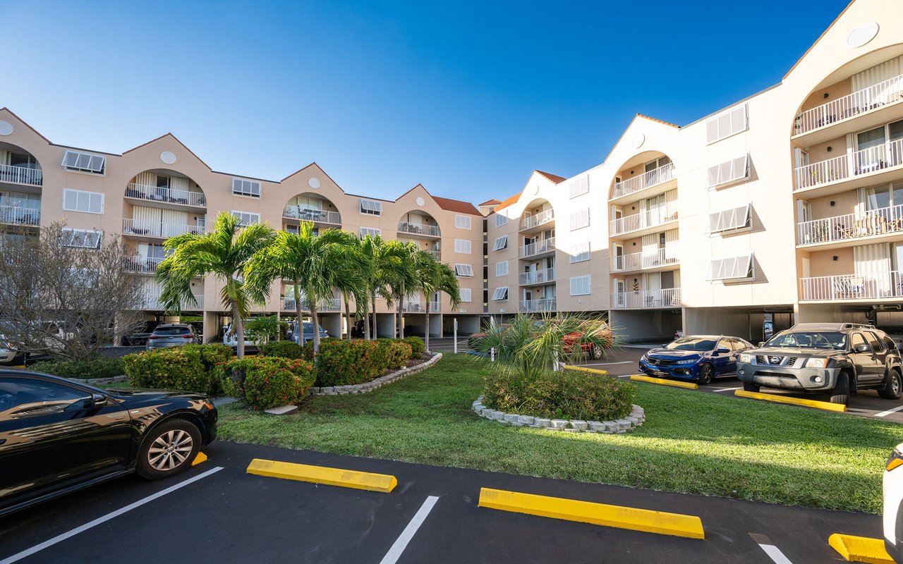 Multi-story condominium buildings with balconies, palm trees, and landscaped parking area.