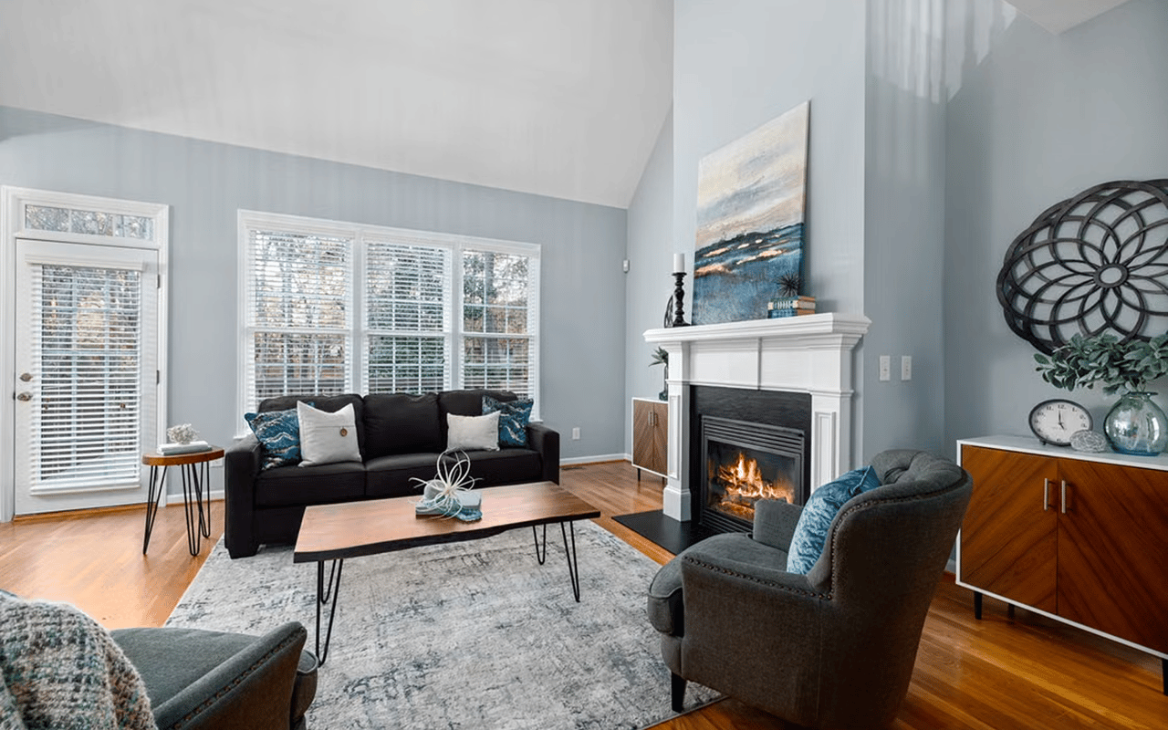 Living room with a lit fireplace, tall windows, and hardwood floors.