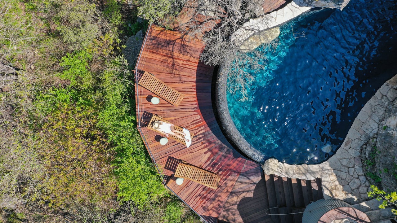 Aerial view of the grotto pool, ipe deck and limestone cliff under the oak canopy, 4002 Tyx Trail, Spicewood, Texas.