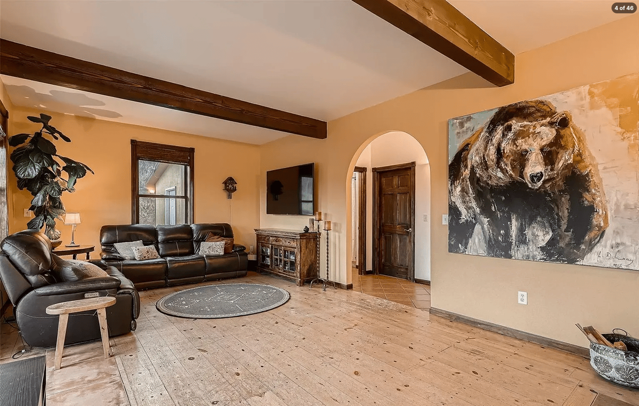 Living room with leather sofas, exposed ceiling beams, distressed wood floors, and a large bear painting.