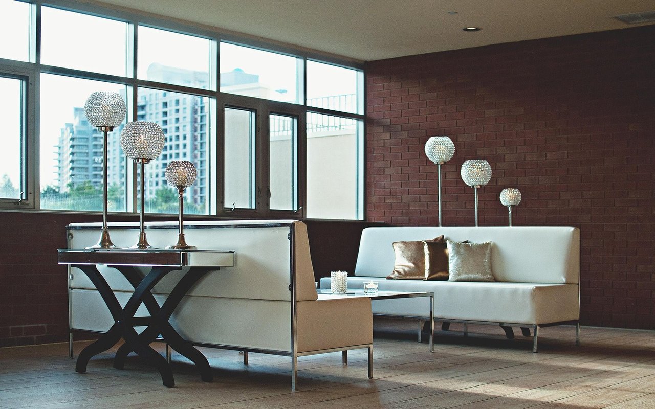 Modern living room with white leather sofas, globe lamps, and large windows overlooking city buildings.