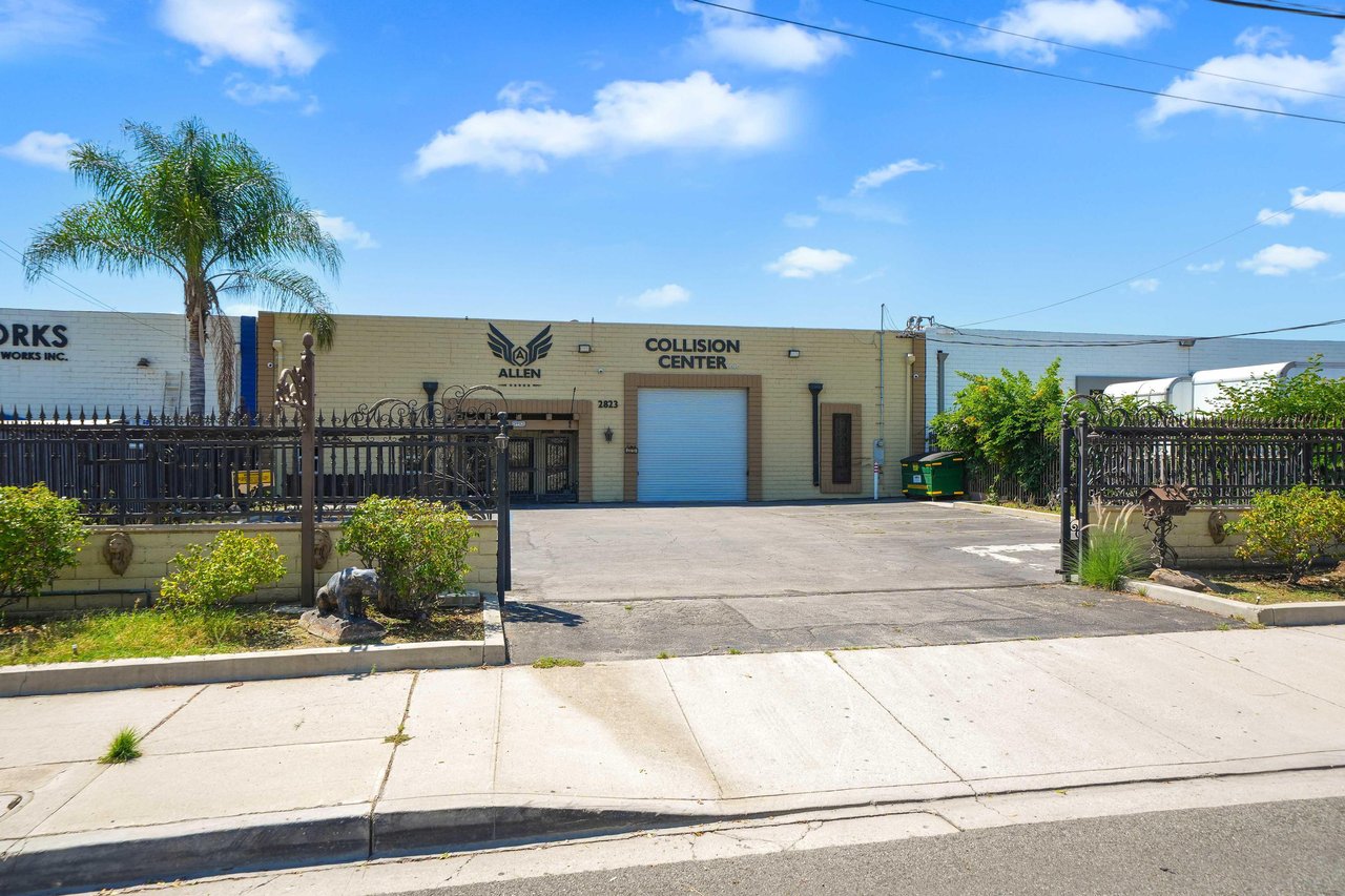 Commercial collision center with a gated driveway, wide garage door, and palm tree.