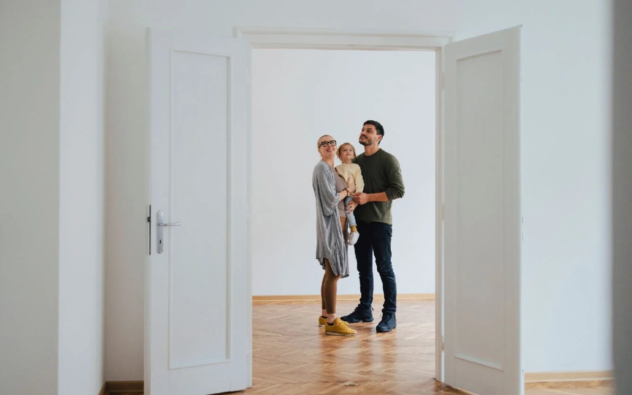 A family stands together in an empty room, looking around through an open doorway.