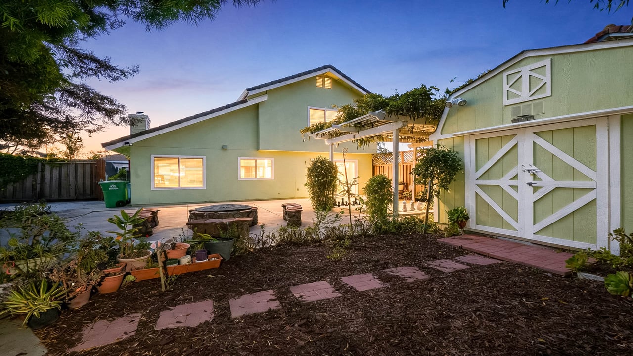 Home’s backyard at dusk with a barn-style garage, pergola patio, and garden path.
