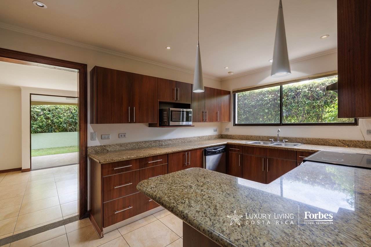 Modern kitchen with dark wood cabinets, granite counters, a large peninsula, and a window overlooking greenery.