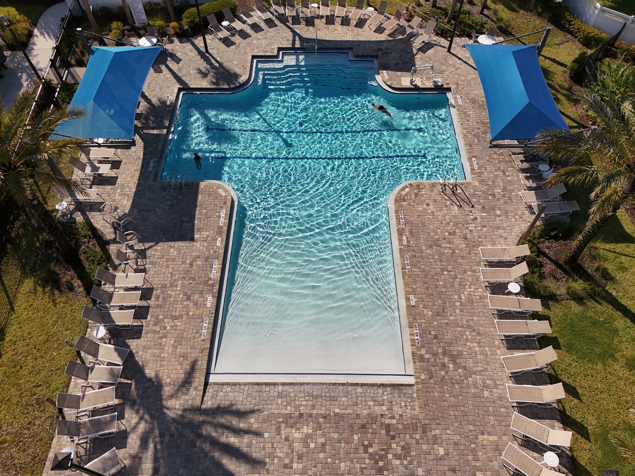 Community swimming pool with swimmers, lounge chairs, and blue shade canopies.