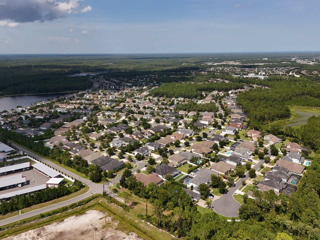 Aerial view of a residential neighborhood with tree-lined streets, a pond, and surrounding woods.