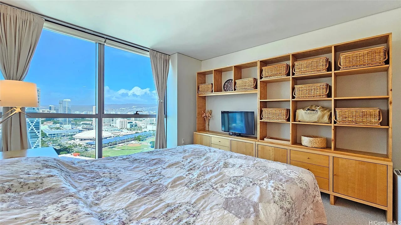 Bedroom with built-in wooden shelving and floor-to-ceiling windows overlooking Honolulu.