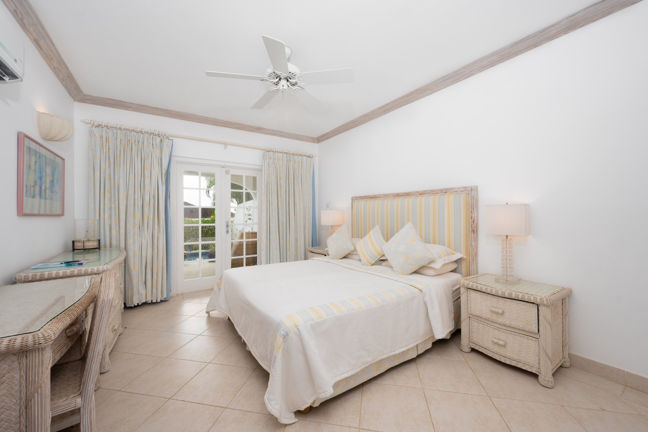 Bedroom with pale yellow striped bedding, woven rattan furniture, and French doors to a patio.