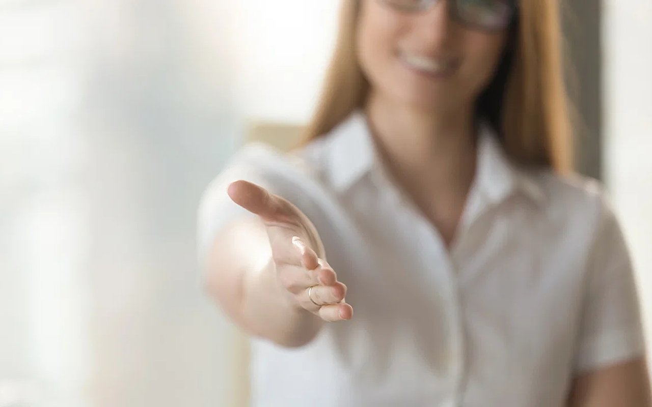 Woman in a white blouse reaches out her hand for a handshake.