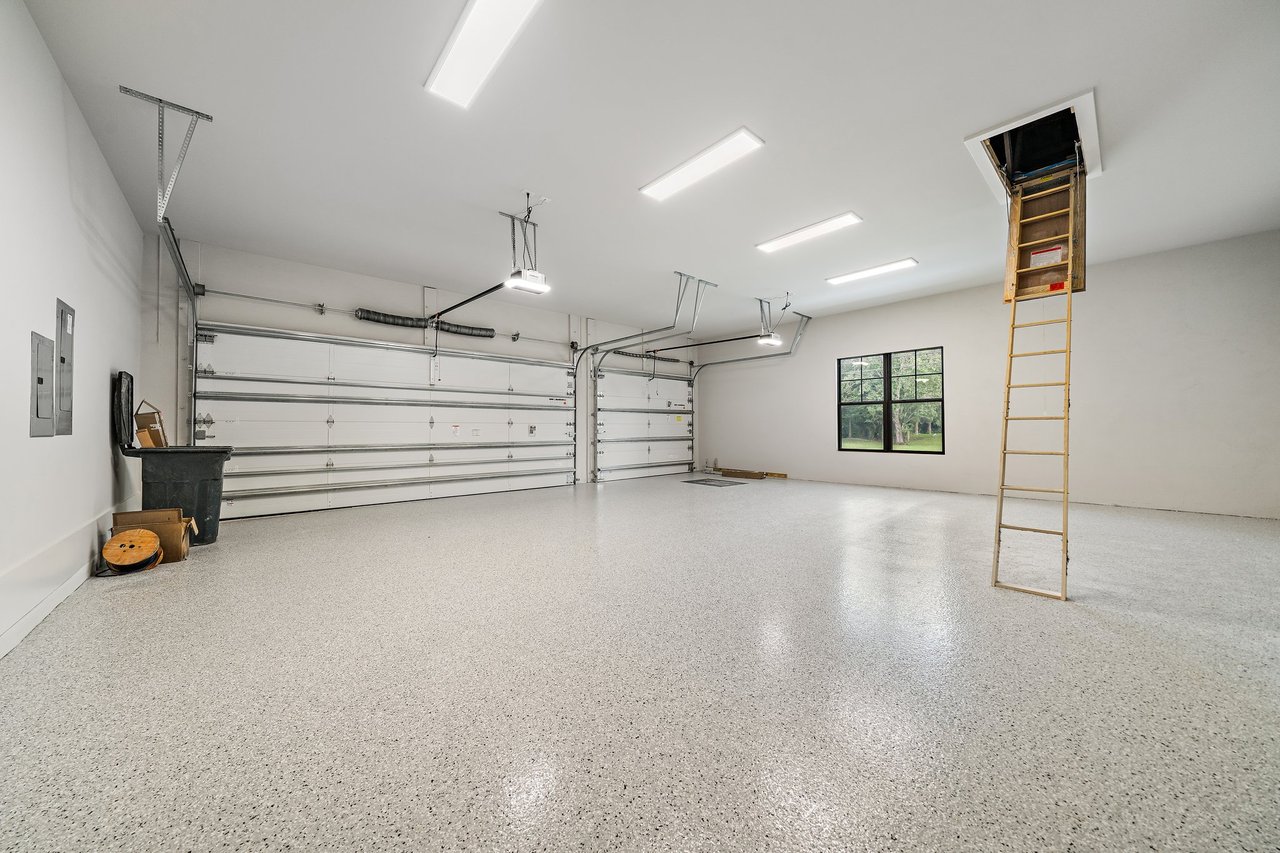 Spacious garage with speckled epoxy flooring, two overhead doors, and a pull-down attic ladder.