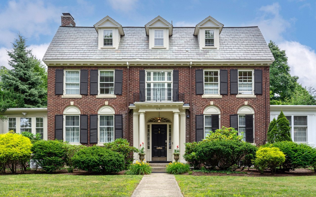 Red brick house with three roof dormers, black shutters, and a columned front entrance.