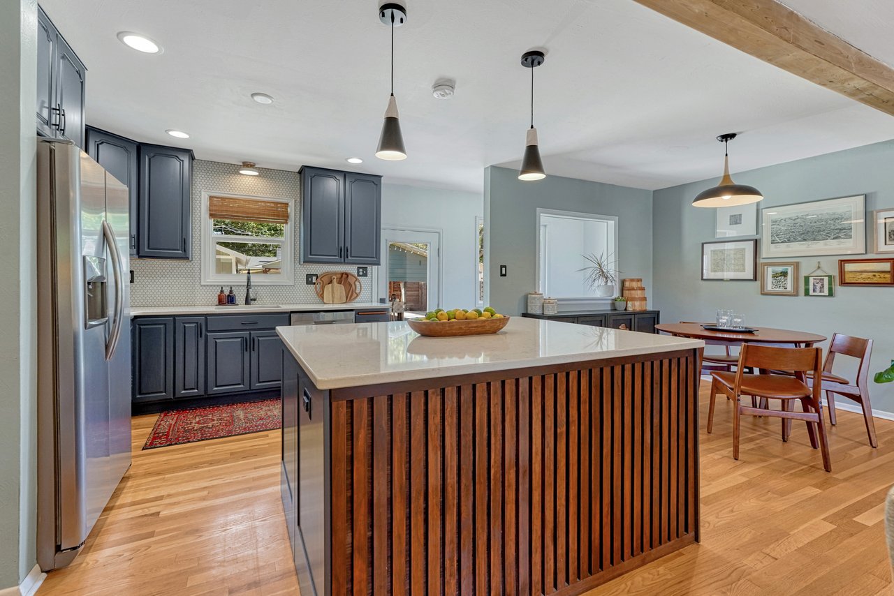 Kitchen with a slatted wood island, gray cabinets and stainless appliances, open to the dining area