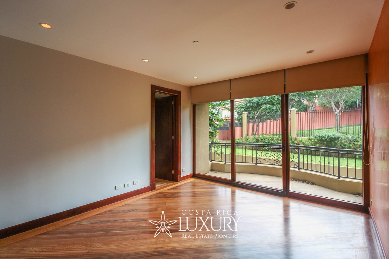Empty apartment room with polished wood floors and sliding glass doors opening to a garden-view balcony.