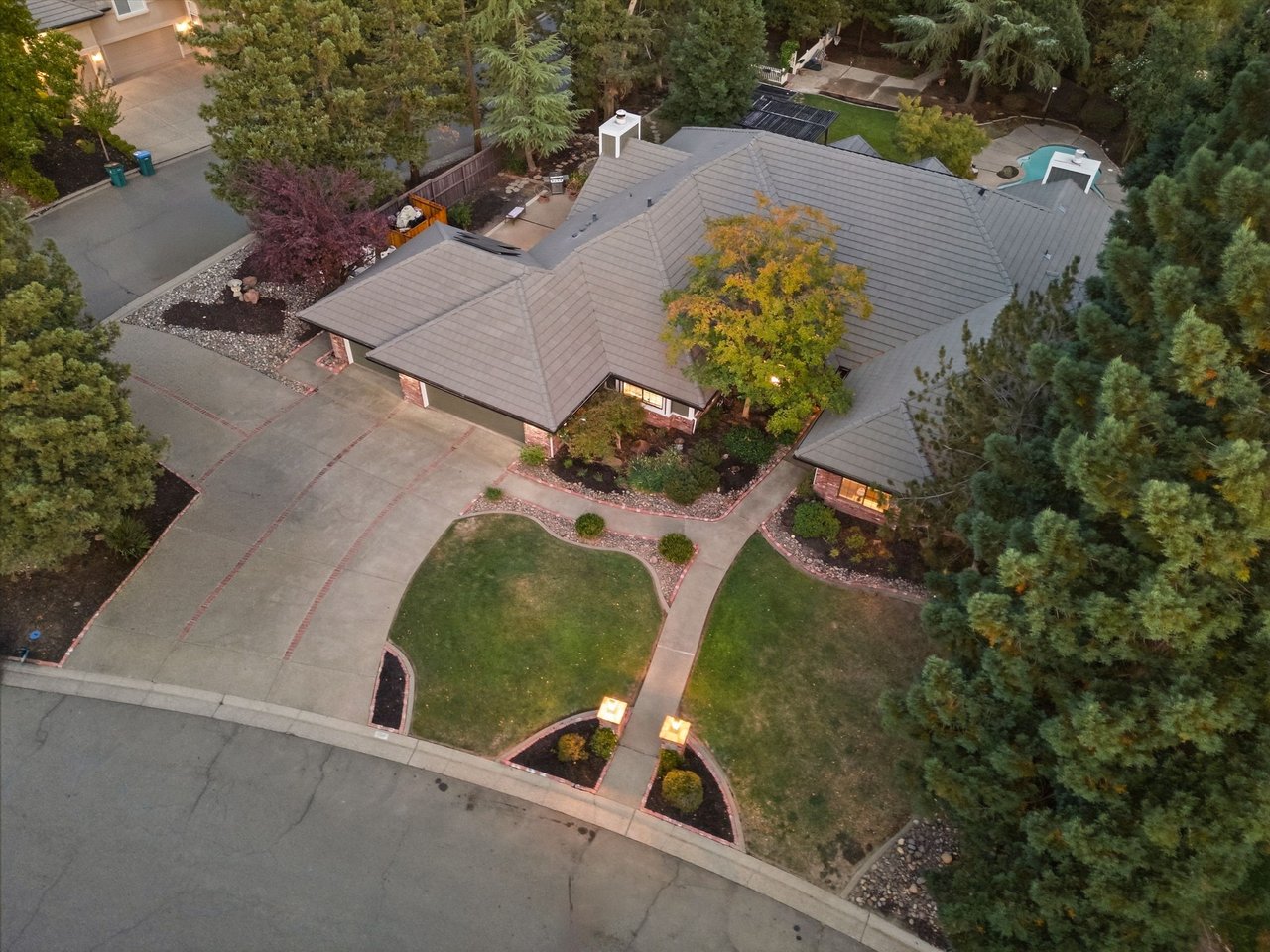 Aerial view of a home with a broad gray tile roof, landscaped yard, and large paved driveway.