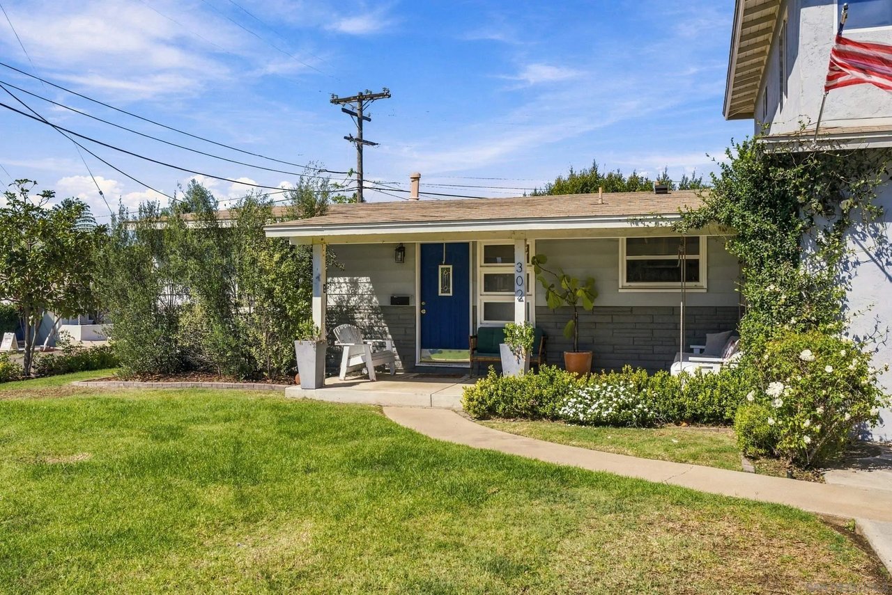 Gray single-story house with a blue door, covered porch, and landscaped lawn.