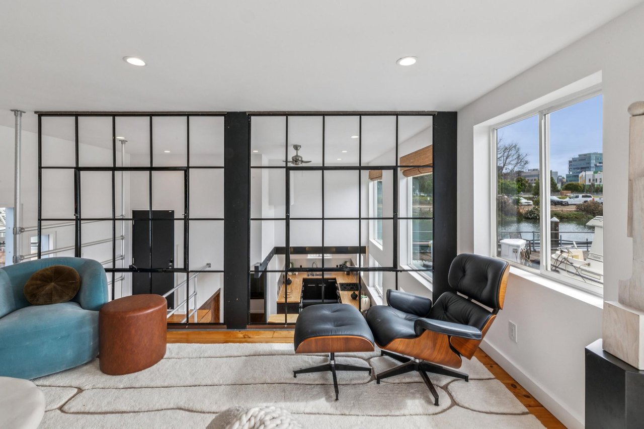Modern living room with black-framed glass partition, leather lounge chair, and water view.