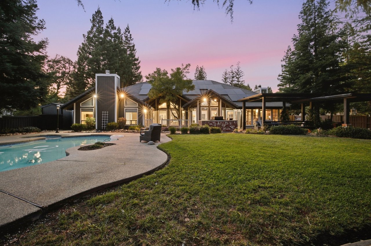 Modern home with solar panels, a swimming pool, and covered patio at dusk.